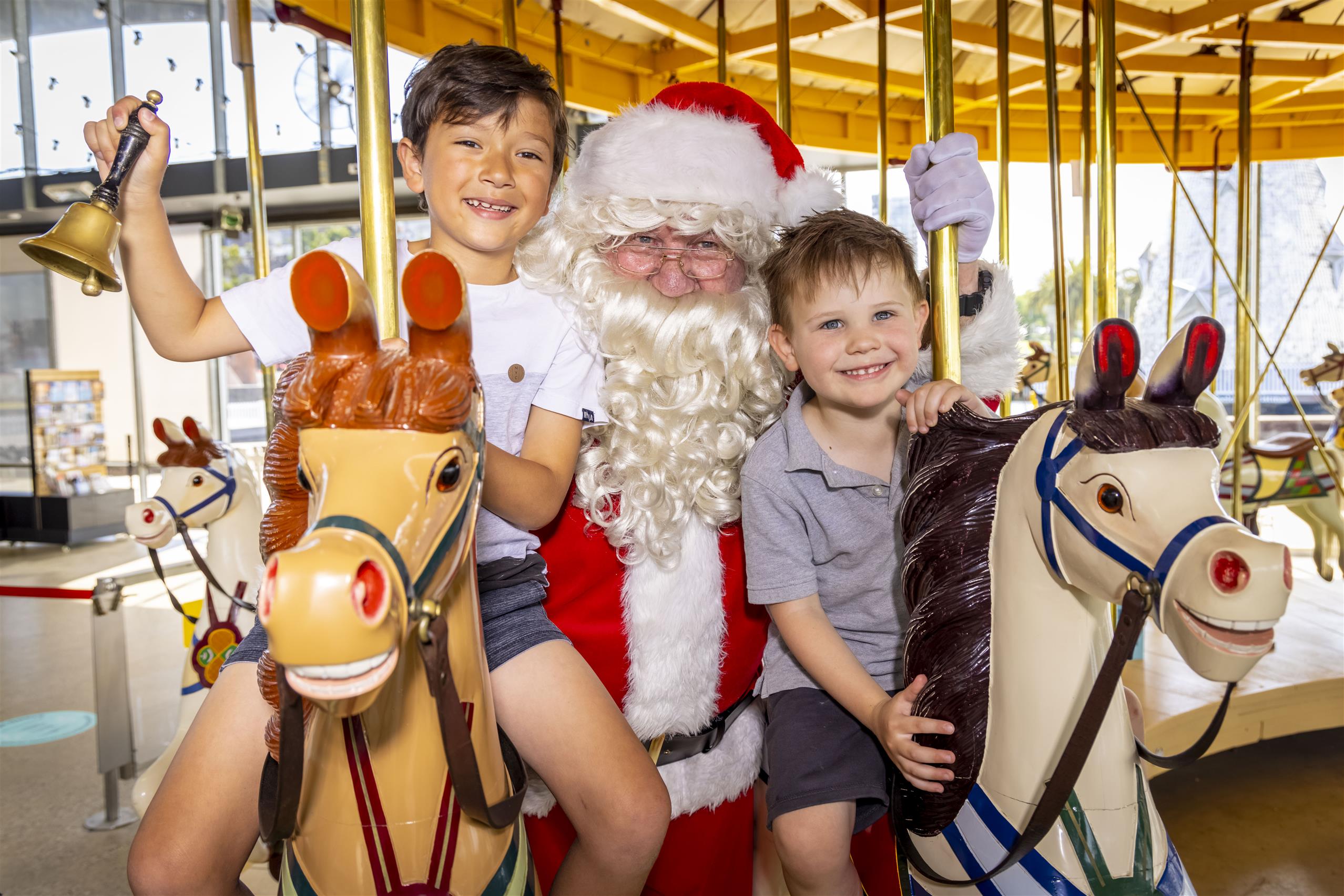 Santa poses on the Carousel horses with two children.