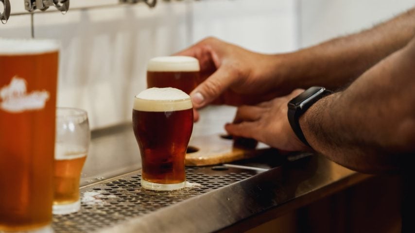 A hand holds beers that are being filled at the tap.