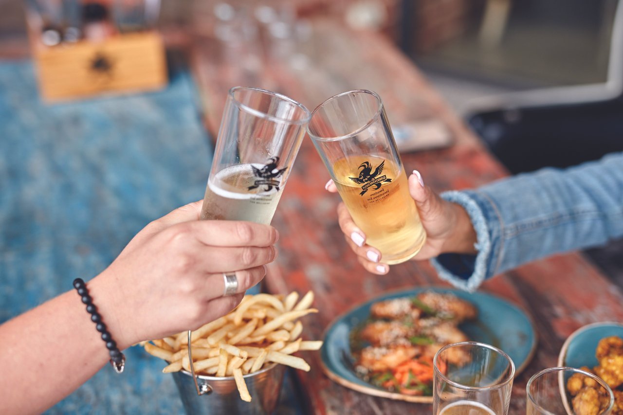 Two people cheers their ciders over a table of food at Flying Brick Cider House.
