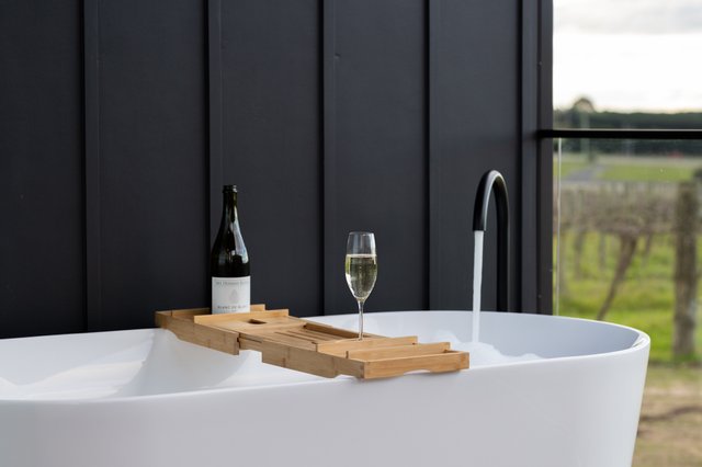 A bath tab fills with water, with a glass and bottle of wine sitting on top of it. The bath is at Mt Duneed Estate winery's accommodation pod.