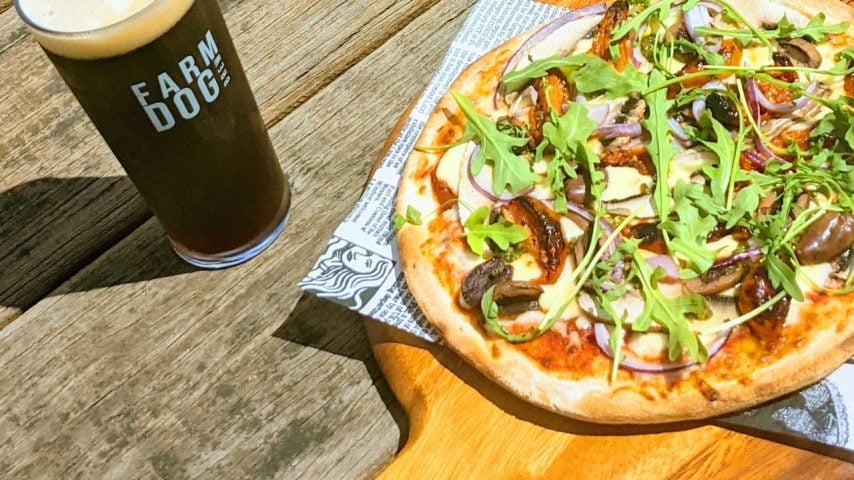 A pizza and dark ale beer sit on a table at FarmDog Brewing.