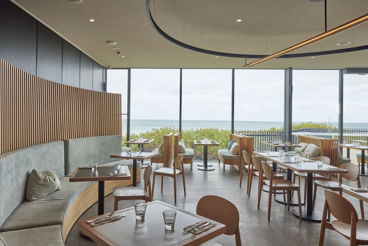 The inside of coastal dining spot The Dunes, which has large windows with views to the surf at Ocean Grove Main Beach.