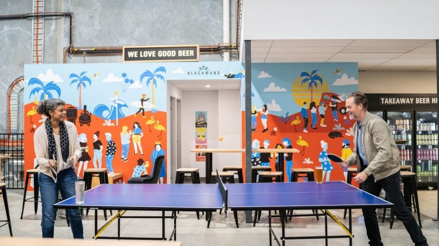 Two people play table tennis at Blackman's Brewery, a mural is behind them that reads "We Love Good Beer".