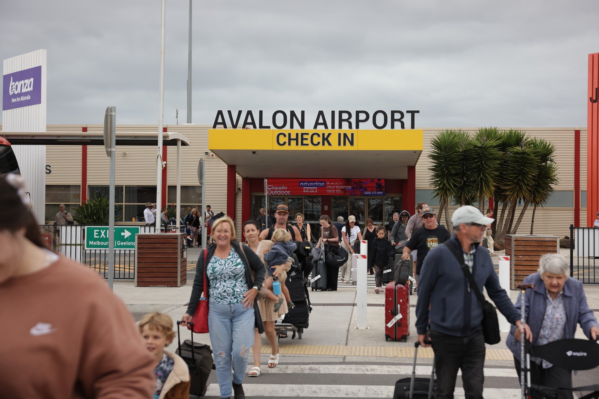 Passengers walk into the entrance of Avalon Airport with their luggage in tow.