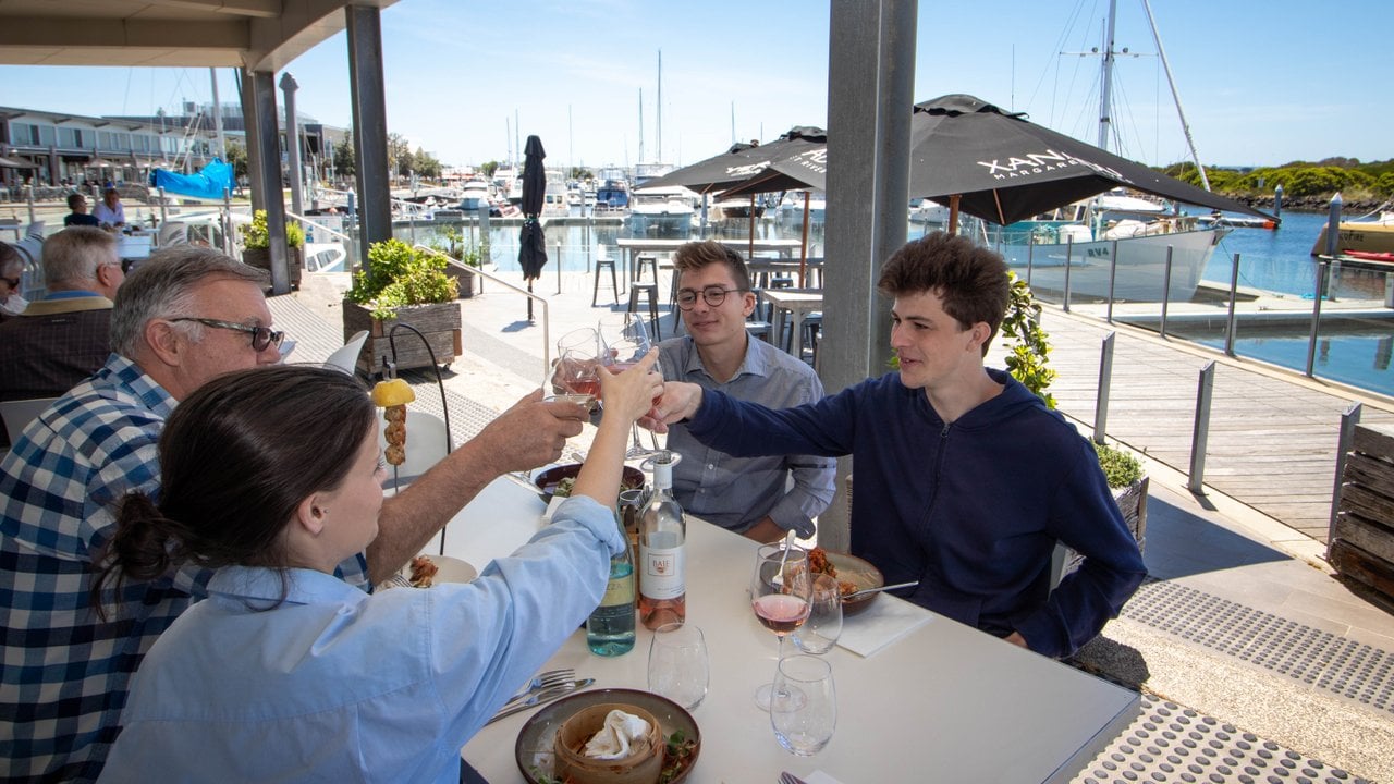 A table of people cheers wine at the outdoor dining at 360Q. The harbour is in the background.