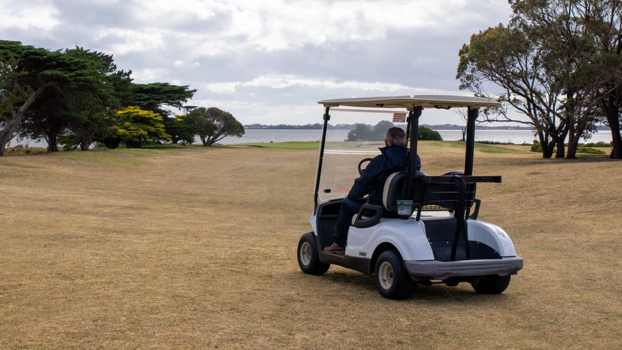 A man sits in a golf buggy overlooking Swan Bay on the course and Queenscliff Golf Club.