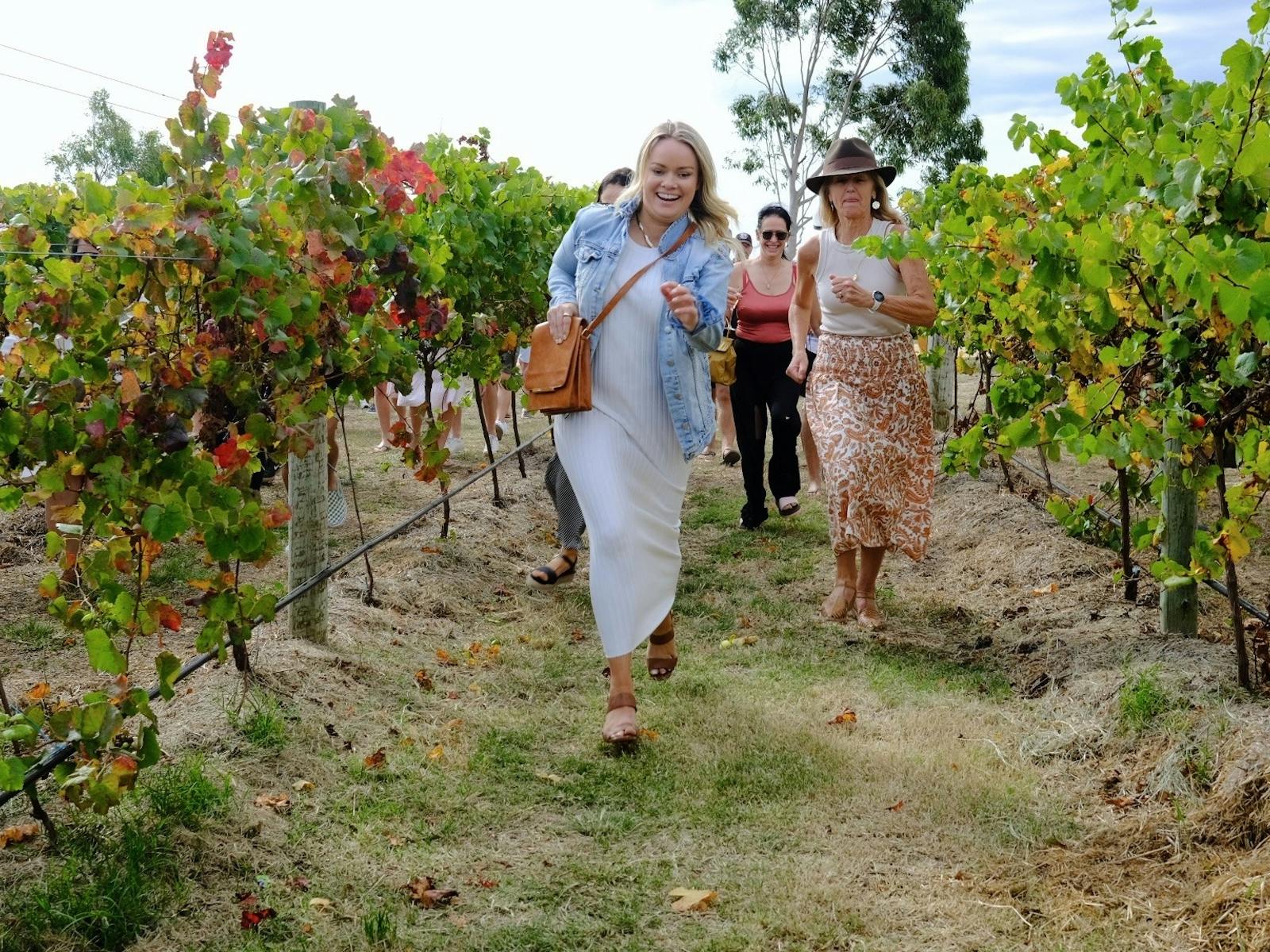 Women run down a vineyard looking for Easter eggs.