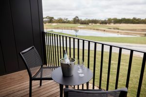 Accommodation balcony with two chairs, a table, a bottle of champagne & two glasses, overlooking a golf course