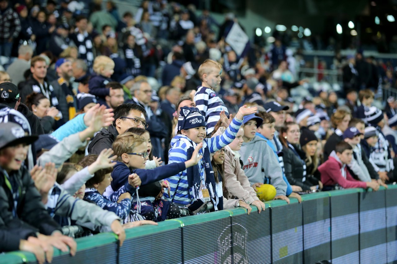 Game day at a Geelong Cats game at GMHBA Stadium, fans cheer the team on the sidelines.