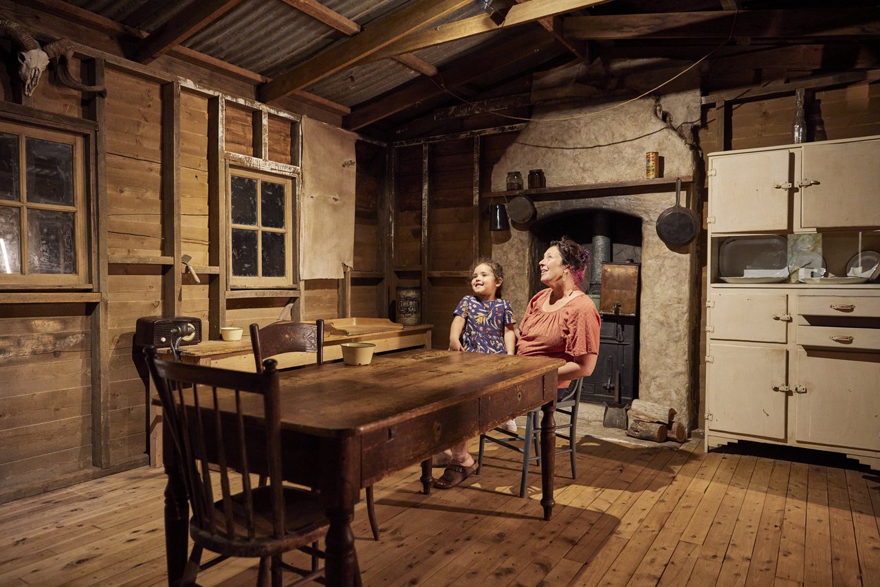 A mother and daughter sit at a table inside a mock older building. At the National Wool Museum