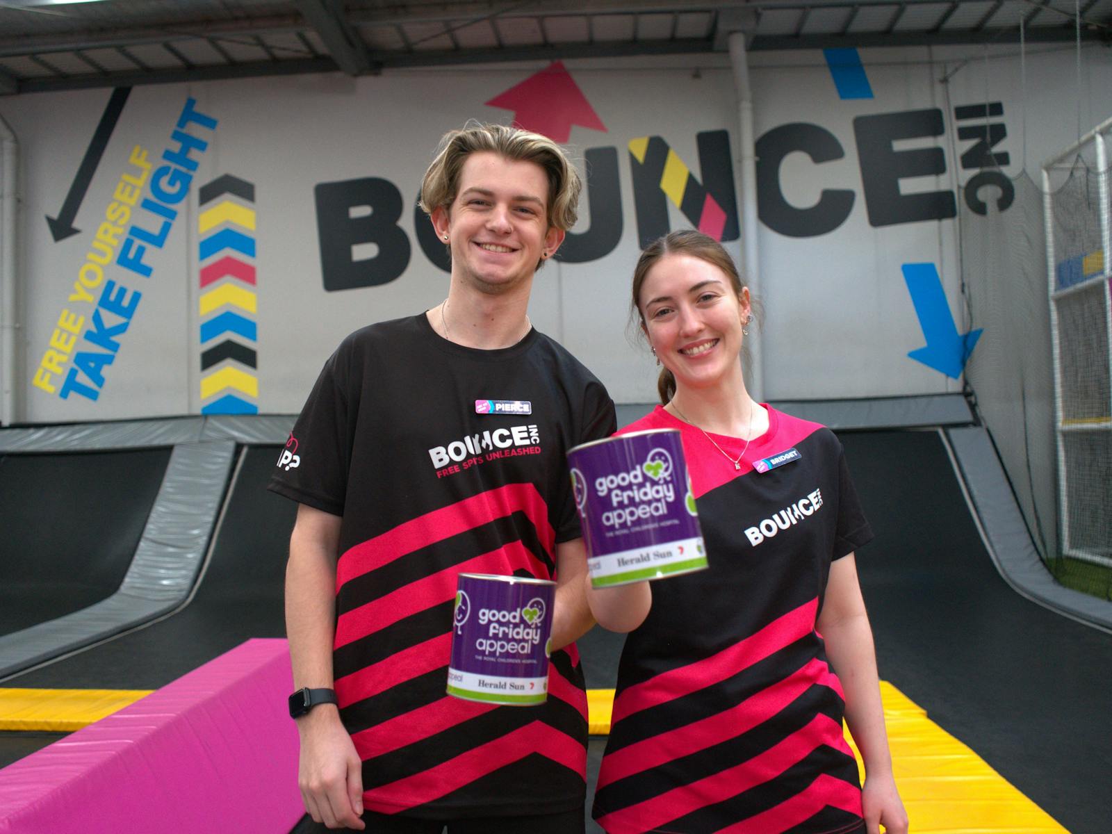 Two workers at Bounce stand next to a trampoline holding Good Friday tins.