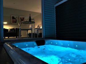 A pool lit up blue with window behind looking into bedroom
